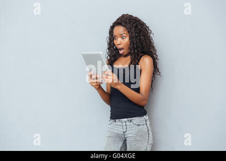 Schockiert Afro Amerikanerin mit Tablet-PC über grauen Hintergrund Stockfoto