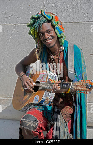 Porträt von einem Straßenmusiker in einem bunten Hut & Outfit spielen & singen auf der Gitarre im Washington Square Park in New York City Stockfoto