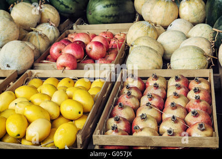 Granatäpfel, Zitronen, Melonen und Äpfel in hölzernen Behältern im Marktplatz. Gesunde Ernährung. Lebensmittel-Markt. Frisches Obst. Stockfoto