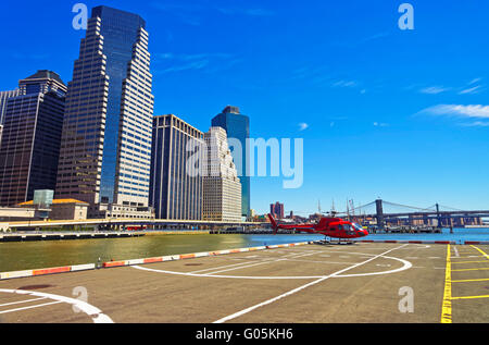 Rot-Hubschrauber am Landeplatz in Lower Manhattan New York, USA, am East River. Pier 6. Wolkenkratzer, Brooklyn Bridge und Manhattan Bridge im Hintergrund Stockfoto