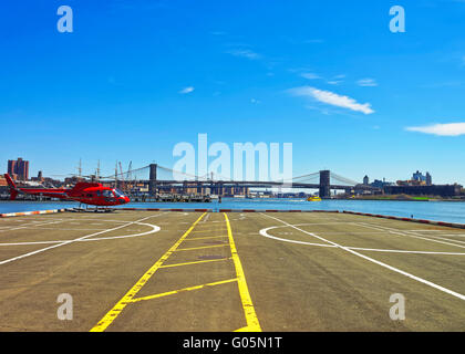 New York, USA - April 25 m 2015: rot Hubschrauber am Landeplatz in Lower Manhattan, New York, USA, am East River. Pier 6. Wolkenkratzer, Brooklyn Bridge und Manhattan Bridge im Hintergrund Stockfoto