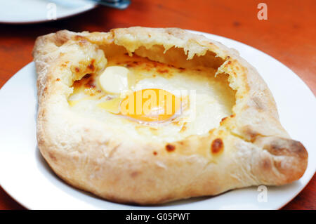 Ajarian oder Adjaruli Khachapuri, gefüllt mit Käse und garniert mit einem rohen Ei und Butter - traditionelles Gericht der georgischen Küche Stockfoto