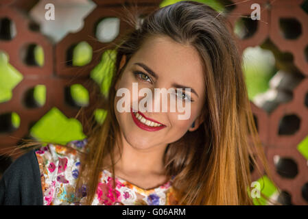 Porträt einer schönen jungen Frau mit großen Lächeln, strahlende Augen und rote Lippen gegen einen Zaun. Geringe Schärfentiefe. Stockfoto