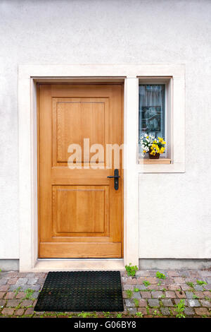 Braun einfache Holztür mit kleinen Fenster auf der Seite gelb weiße Blume auf der Fensterbank Stockfoto