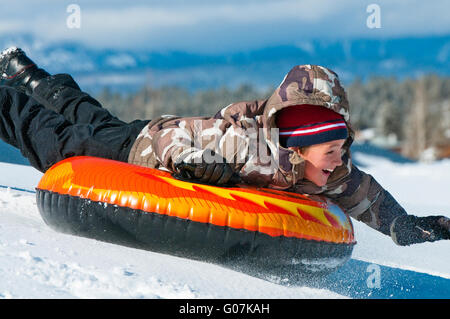 Fröhlicher Junge Reiten ein Rohr im Schnee Stockfoto