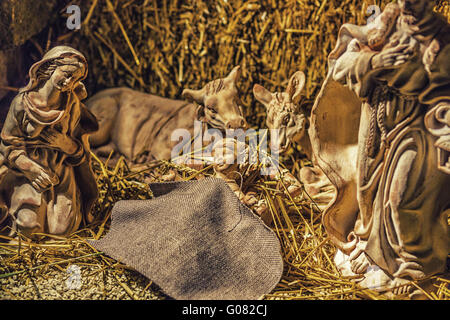 Statuen in eine Weihnachtskrippe, der seligen Jungfrau Maria und St. Joseph wachen über die Heiligen Jesuskind in einer Krippe in das Stroh wie der Ochse und der Esel Erwärmung Stockfoto