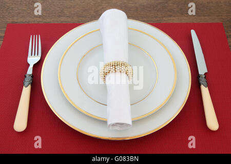 Elegante Tischdekoration mit Weißgold umrandeten Porzellanteller, antikes Besteck, Bettwäsche Serviette mit Ring am Roten Platz-Matte. Stockfoto