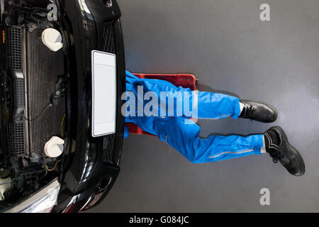 Mechaniker in blauer Uniform hinlegen und arbeiten unter dem Auto in der Garage. Stockfoto