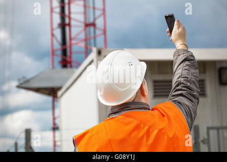 Mitarbeiter mit dem Handy in der Nähe von GSM-Turm Stockfoto