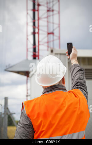 Mitarbeiter mit dem Handy in der Nähe von GSM-Turm Stockfoto