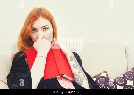 Junge rothaarige Frau mit rotem Einband Bücher sitzend auf Sofa-Porträt Stockfoto