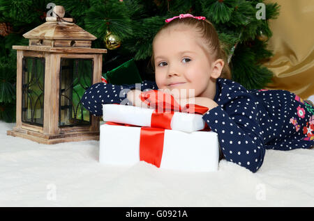 Das kleine Mädchen auf einem Fell-Weihnachtsbaum mit Geschenken Stockfoto