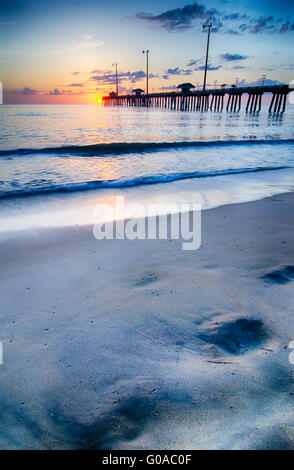 Die aufgehende Sonne lugt durch die Wolken und spiegelt sich in Wellen von dem Nags Head Fishing Pier auf den outer Banks von North Carolina Stockfoto