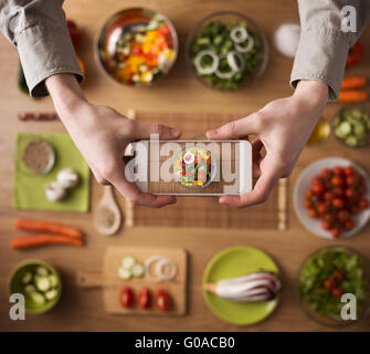 Mann hält ein Smartphone Hände nahe bis Tabelle Küchenarbeitsplatte auf Hintergrund mit frischem Gemüse und Geschirr Stockfoto