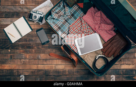 Vintage Hipster Reisenden Verpackung, offene Koffer auf einem Holztisch mit Kleidung, Kamera und Handy, Ansicht von oben Stockfoto