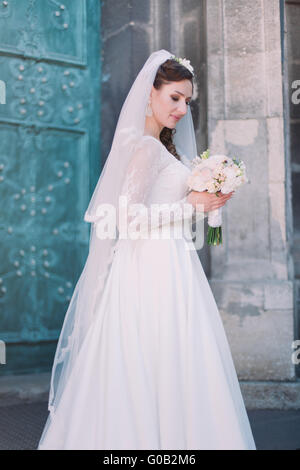 Lächeln schöne Braut an Ihrem Hochzeitstag mit großen Blumenstrauß in der Nähe von Kirche. Grüne alte Tür. Stockfoto