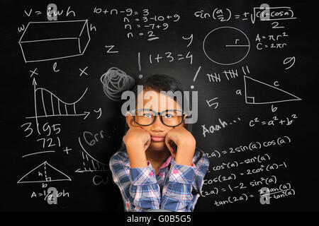 Kleine asiatische Studentin Mädchen mit Brille zeigt gelangweilt und müde über grüne Tafel mit Mathe-äquivalente darauf geschrieben Stockfoto