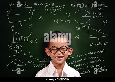 Kleine Genies asiatische Studentin junge mit Brille lächelnd über grüne Tafel mit Mathe-äquivalente darauf geschrieben Stockfoto