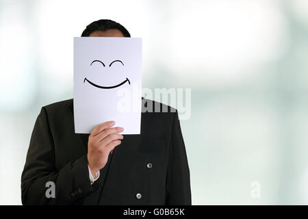 Firmen-Konzept-Image eines Geschäftsmannes halten weiße Papier-Maske mit glücklich lächelnden Gesicht drauf gezogen Stockfoto