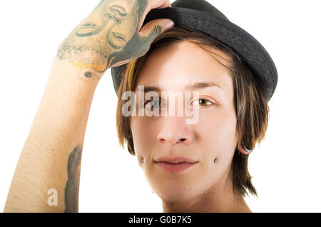 Kopfschuss jungen hispanischen männlichen tragen schwarzen Hut, rote Tunika Shirt mit Tattoos auf der Brust und Arme, Punk Rock inspiriert-Look, posiert für die Kamera Stockfoto