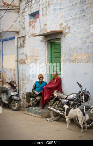 Zwei ältere Männer sitzen vor Haustür des blauen Hauses in Jodhpur Stockfoto