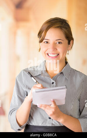 Junge Brünette Kellnerin mit freundlichen Lächeln die Bestellung schriftlich auf Notepad, Restaurant Hintergrund Stockfoto