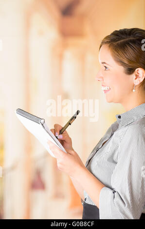 Junge Brünette Kellnerin mit freundlichen Lächeln die Bestellung schriftlich auf Notepad, Restaurant Hintergrund Stockfoto