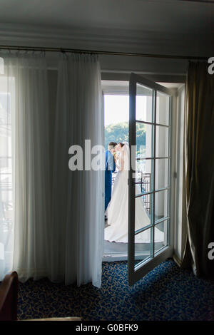 Schöne junge Braut und Bräutigam küssen auf dem Balkon im Hotelzimmer Stockfoto