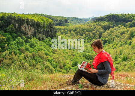 Frau liest ein Buch über Blumen mit einem schönen Wald-Hintergrund Stockfoto