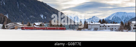 Roter Zug durch Davos Dorf im Winter mit Schnee bedeckt Alpen im Hintergrund Stockfoto
