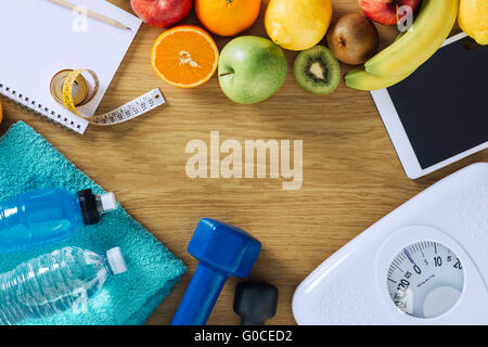 Fitness und Gewicht-Verlust-Konzept, Hanteln, weiße Skala, Handtücher, Obst, Maßband und digital-Tablette auf einem Holztisch Stockfoto