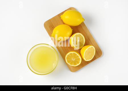 Schüssel mit frisch gepressten Zitronensaft und reife Zitronen auf Holzbrett Stockfoto