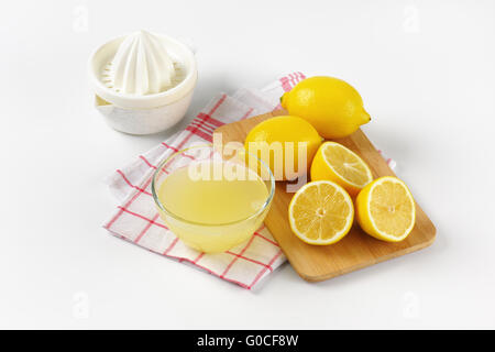 Schüssel mit frisch gepressten Zitronensaft, Zitronenpresse und reife Zitronen auf Holzbrett Stockfoto