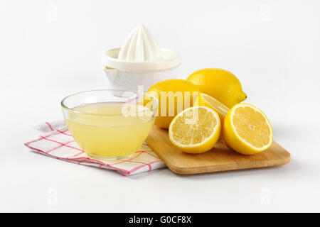 Schüssel mit frisch gepressten Zitronensaft, Zitronenpresse und reife Zitronen auf Holzbrett Stockfoto