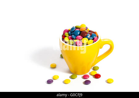 Bunte Dragees in kleinen gelben farbigen Tasse auf weiß Stockfoto