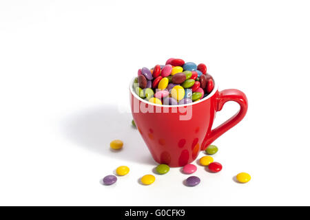 Bunte Dragees in kleinen roten farbigen Tasse auf weiß Stockfoto