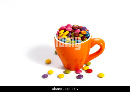 Bunte Dragees in kleinen orange farbigen Tasse auf weiß Stockfoto