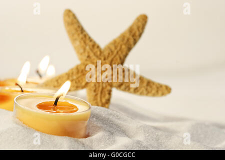 Orange Teelichter in Sand mit Seestern Stockfoto