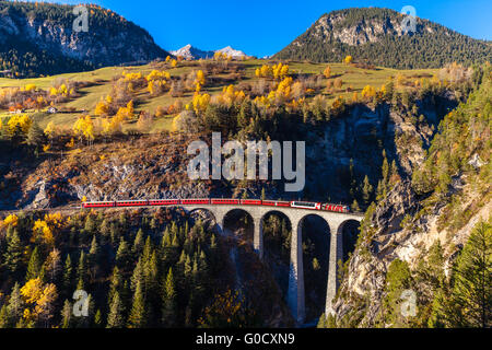 Der Zug der Rhätischen Bahn laufen auf dem berühmten Landwasser Viadukt in den Tunnel, mit Blick auf bunte Bäume an einem sonnigen Stockfoto