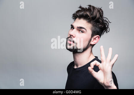 Junger Mann im schwarzen T-shirt zeigt Geste ok Stockfoto