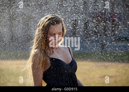 Junge Frau nimmt eine Erfrischung unter einem sprinkler Stockfoto