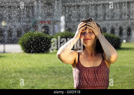 Junge Frau nimmt eine Erfrischung unter einem sprinkler Stockfoto