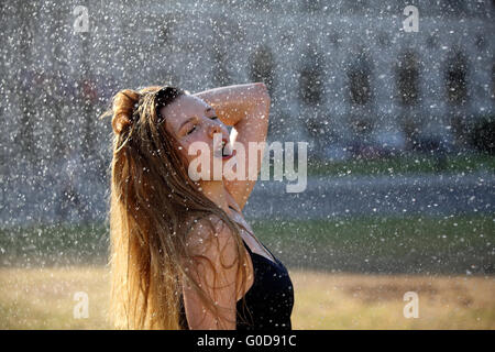 Junge Frau nimmt eine Erfrischung unter einem sprinkler Stockfoto