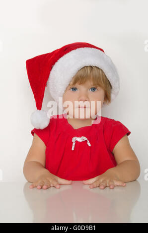 kleines Mädchen im Kostüm des Weihnachtsmannes am Tisch Stockfoto