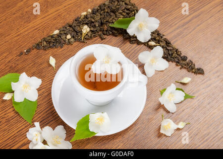 weiße Tasse mit Untertasse mit Jasminblüten auf einem Holztisch. Ansicht von oben Stockfoto