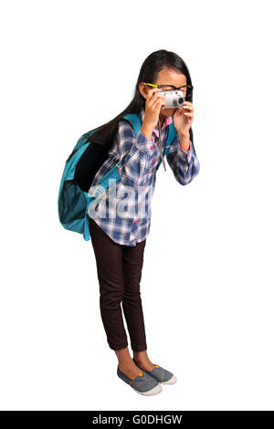 Kleines Mädchen mit Brille und Rucksack stehen und unter Foto mit ihrer Kamera isoliert auf weiss Stockfoto