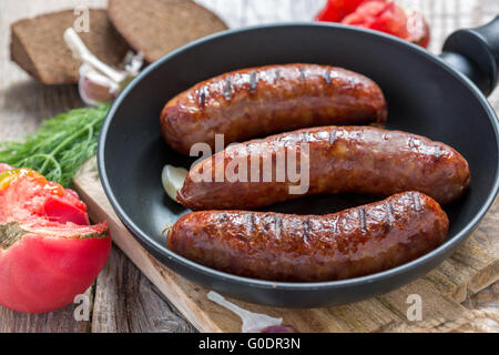 Gegrillte Würstchen in die Pfanne geben und eine reife Tomate. Stockfoto