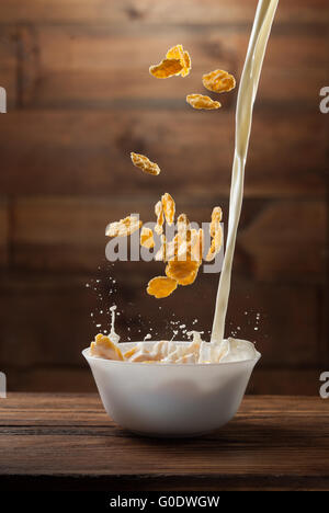 Fallende Cornflakes mit Milch Spritzen auf Holz Stockfoto