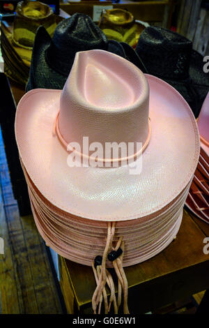 Ein Stapel von rosa Cowboy Strohhüte sitzt auf einer Anzeigetabelle unter Hunderten von Cowboy-Stiefel in Nashville Cowboy Store, TN Stockfoto