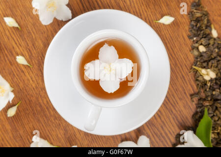 weiße Tasse mit Untertasse mit Jasminblüten auf einem Holztisch. Ansicht von oben Stockfoto